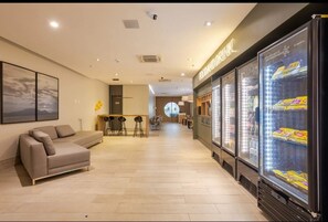 A modern hotel lobby with a sofa, bar area, and refrigerated display cases. - SHB - 200m Praia Studio Moderno Gonzaga (Santos)