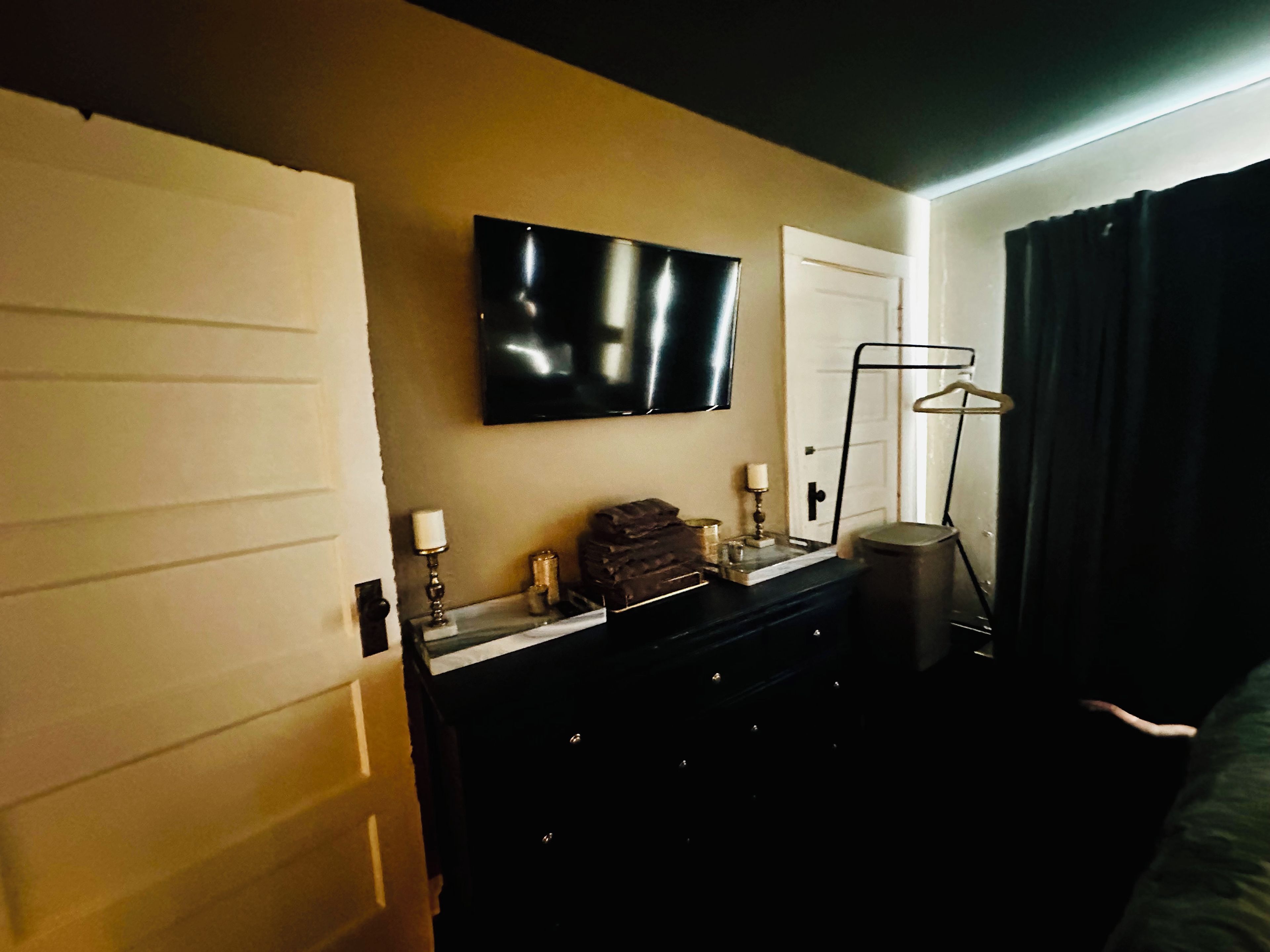 Ein Hotelzimmer mit einem wandmontierten Flachbildfernseher, einem Schminktisch mit Spiegel, einem Kleiderständer und einer Mülleimer.