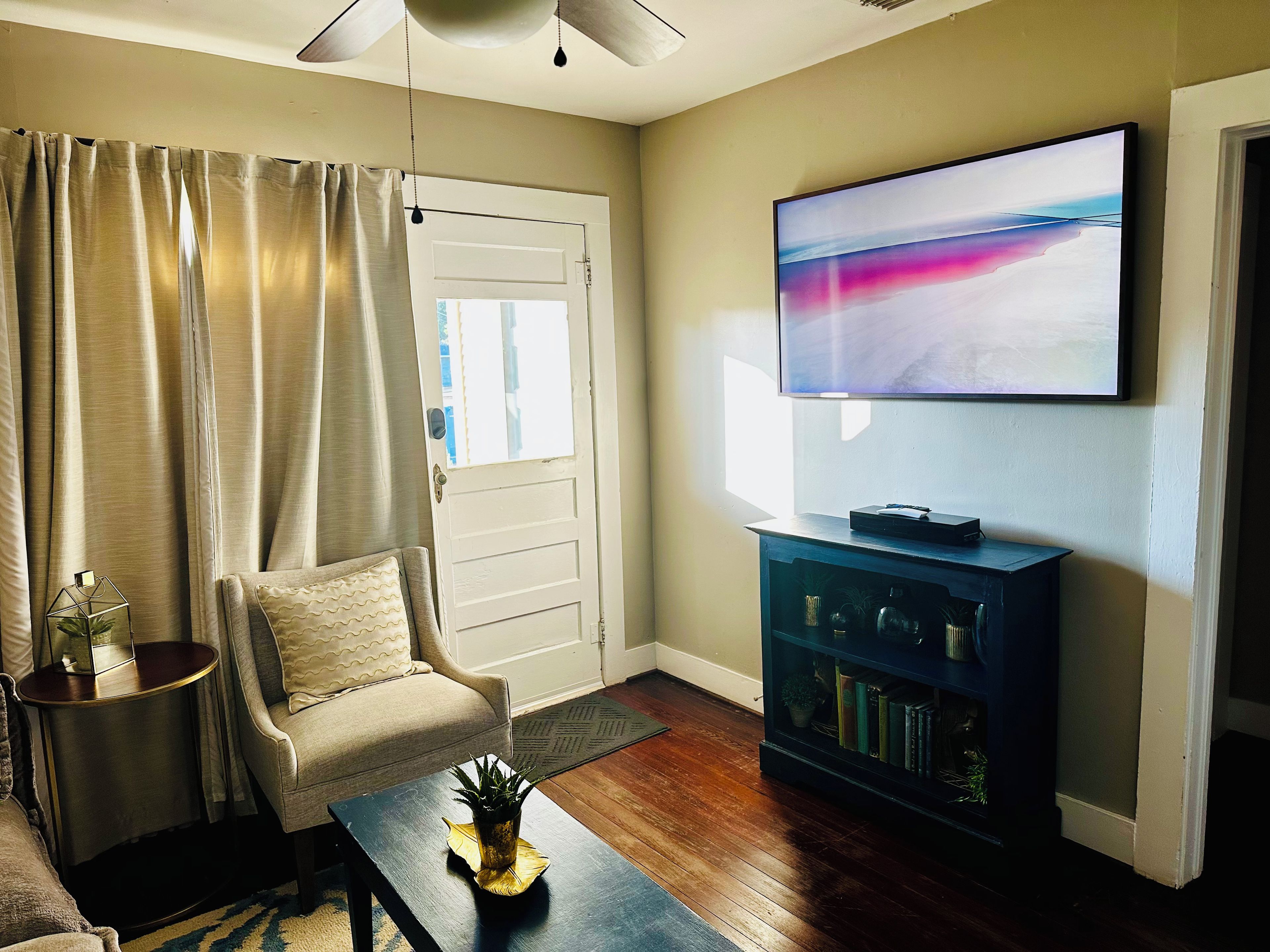 A living room with a sofa, a coffee table with a plant, a television on a stand, and a door with curtains.