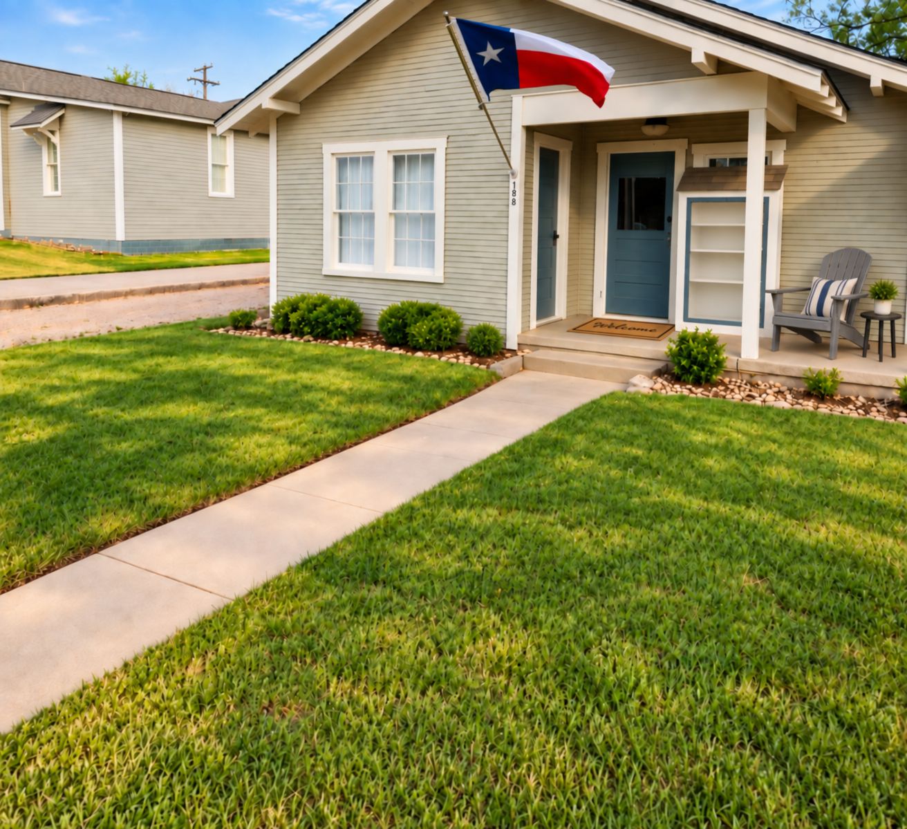 A residential house with a front porch, a flag, and a well-maintained lawn.