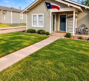 A residential house with a front porch, a flag, and a well-maintained lawn.