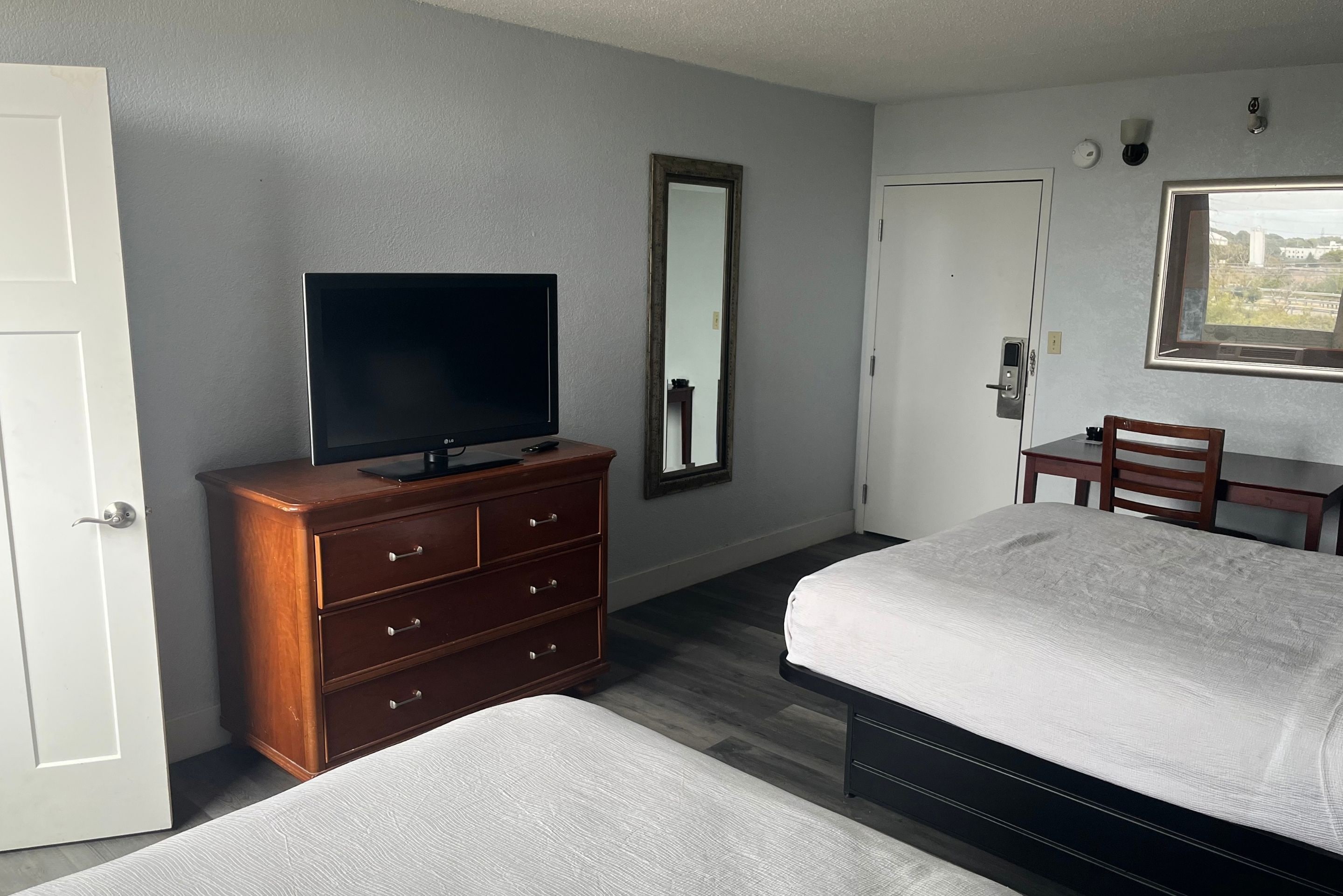 Een hotelkamer met een bed, een kaptafel, een televisie, een spiegel, een bureau en een raam met uitzicht.