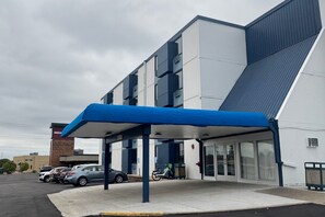 Un bâtiment moderne doté d’une entrée couverte, d’un parking où sont garées plusieurs voitures et d’un ciel dégagé.