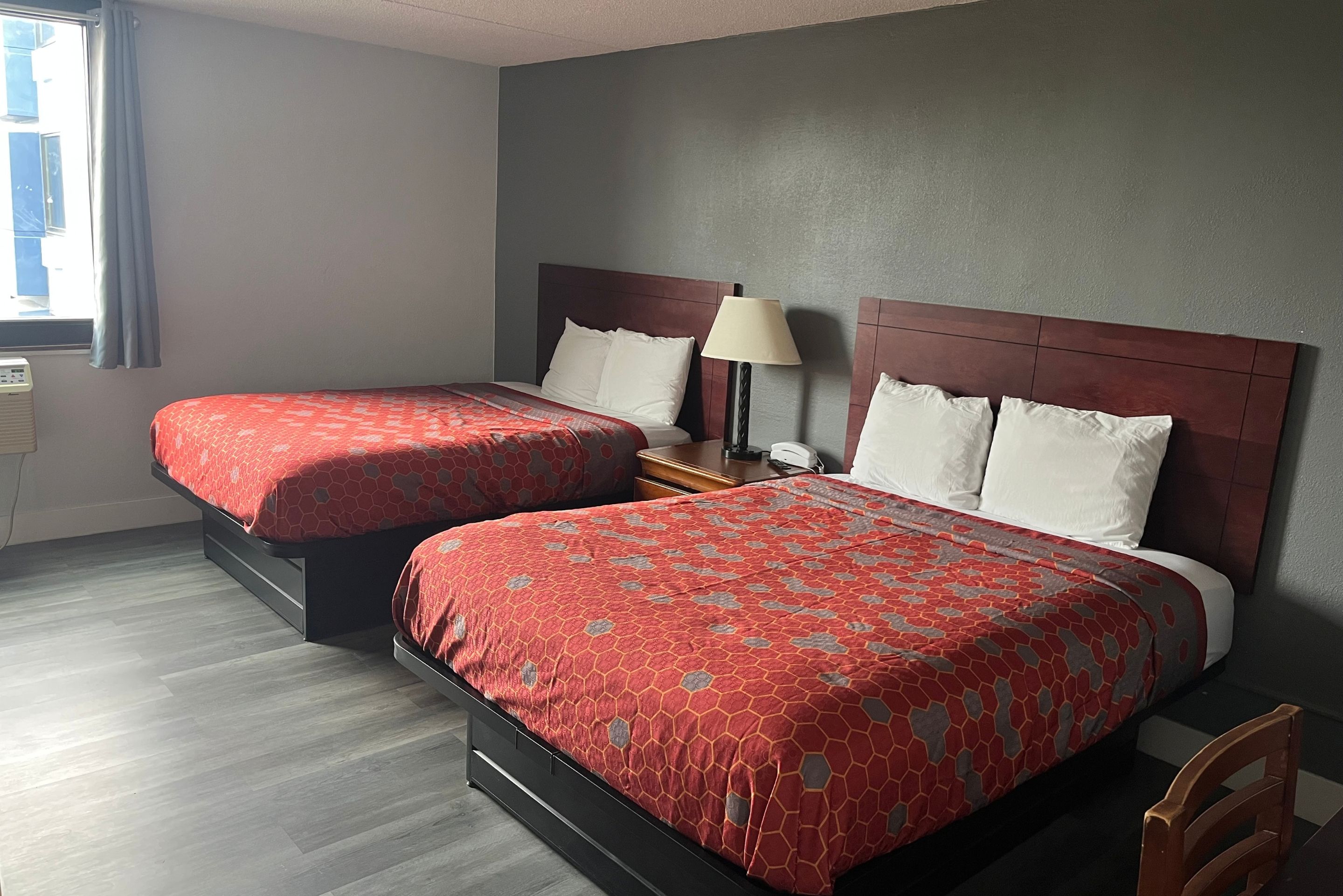 Habitación de hotel con dos camas, una mesita de noche, una lámpara y una ventana con cortinas.