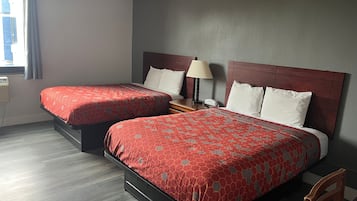 Habitación de hotel con dos camas, una mesita de noche, una lámpara y una ventana con cortinas.
