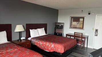 A hotel room with two beds, a desk, a chair, a microwave, and a framed picture on the wall.