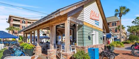 A brick building with a covered patio area, outdoor seating, and a sign for 'Kickstands Cocktails & Coffee.'