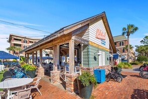 A brick building with a covered patio area, outdoor seating, and a sign for 'Kickstands Cocktails & Coffee.' - Good Day Sunshine by Stay on 30a (Seacrest Beach)