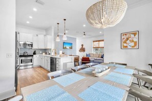 A modern kitchen with white cabinets, stainless steel appliances, and a dining area with a wooden table and blue placemats. - Good Day Sunshine by Stay on 30a (Seacrest Beach)