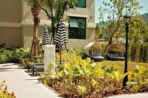 A landscaped outdoor area with a palm tree, striped umbrellas, a round seating area, and a lamp post. - Bang Tao - Terrace by the Pool (Tambon Choeng Thale)
