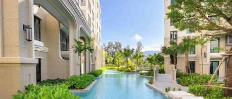A swimming pool flanked by buildings with balconies and lush greenery.