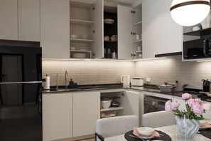 A modern kitchen with built-in appliances, a dining area with a vase of flowers, and a large island with storage. - Bang Tao - Terrace by the Pool (Tambon Choeng Thale)