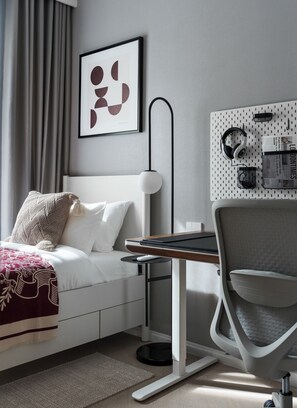 A modern hotel room with a neatly made bed, a desk with a chair, a wall-mounted pegboard with headphones and a newspaper, and a framed abstract artwork. - Bang Tao - Terrace by the Pool (Tambon Choeng Thale)