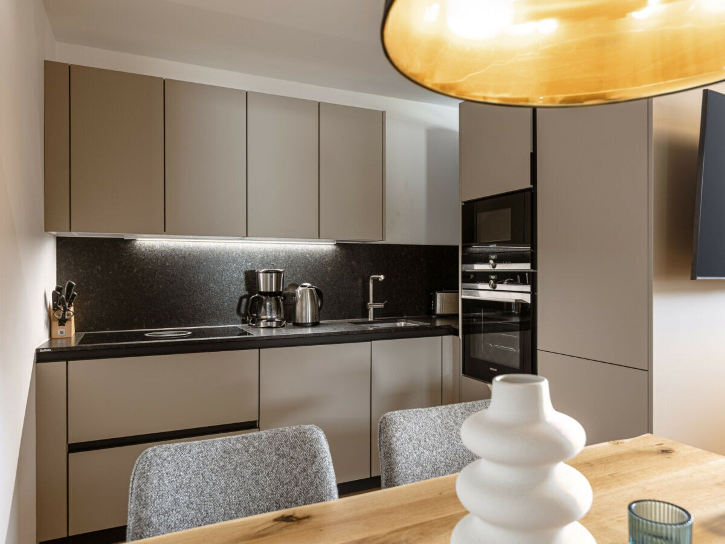A modern kitchen with a black countertop, stainless steel appliances, and a wooden dining table with chairs.