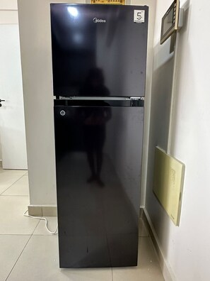 Un refrigerador negro con una etiqueta de garantía, ubicado en una habitación con paredes blancas y piso de baldosas.