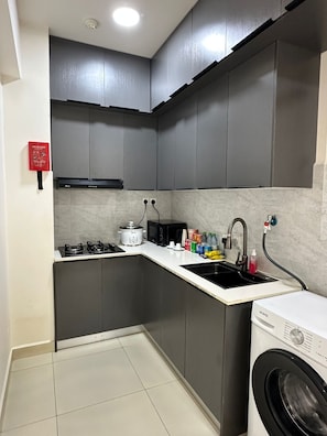 Cocina compacta con armarios grises, estufa a gas, microondas, pileta y lavadora.