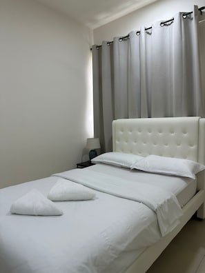 A single bed with a tufted headboard, white bedding, and a nightstand with a lamp.