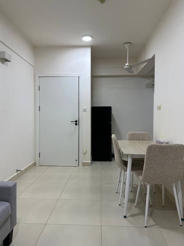 A room with a closed door, a ceiling fan, a table with chairs, and a tiled floor.