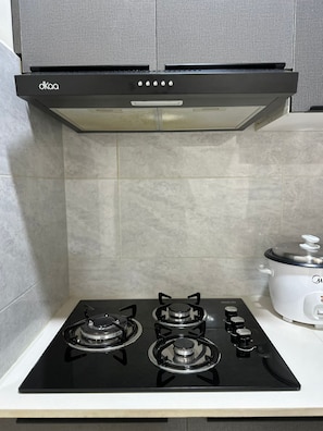 A kitchen with a black gas stove, a white slow cooker, and a grey range hood.