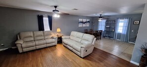 A living room with a sofa, a lamp, a ceiling fan, and a dining area with a table and chairs.