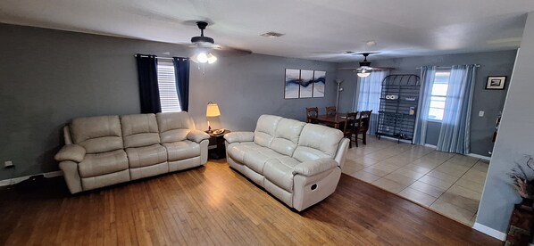 A living room with a sofa, a lamp, a ceiling fan, and a dining area with a table and chairs.
