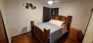 A bedroom with a wooden bed, a nightstand, a dresser, and a wall decoration.