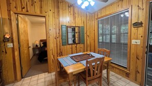 Una stanza con rivestimento in legno, un tavolo da pranzo, sedie, una ventola a soffitto e una finestra con persiane.