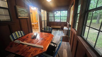 A wooden dining table with chairs, a ceiling fan, and large windows with a view of the outdoors.