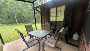 Un'area patio coperta con tavolo e sedie, un barbecue e vista sul verde circostante.