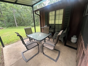 Ein überdachter Patio-Bereich mit Tisch und Stühlen, einem Grill und Blick auf die umliegende Grünfläche.