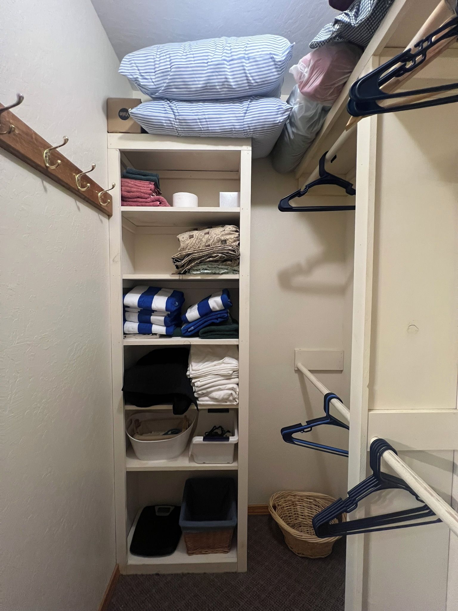 A narrow walk-in closet with shelves for folded clothes, a hanging rack, and a shoe rack.