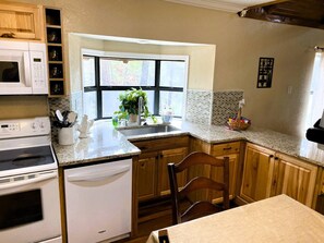 A kitchen with a built-in oven, microwave, and dishwasher, a window with a view, and wooden cabinets. - Carter Creek Retreat - Ride to trails! (Mena)