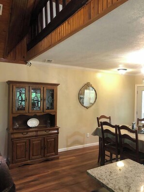 A dining area with wooden chairs and a table, a wooden cabinet with glass doors, and a mirror on the wall. - Carter Creek Retreat - Ride to trails! (Mena)
