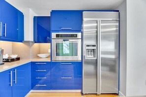 A modern kitchen with blue cabinets, a stainless steel refrigerator, and an oven. - W Penthouse | Ocean Views | Rooftop Pool (Fort Lauderdale)