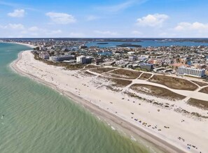 Vista aerea di una città costiera con un'ampia spiaggia, acque blu cristalline e una zona urbana densa con edifici.