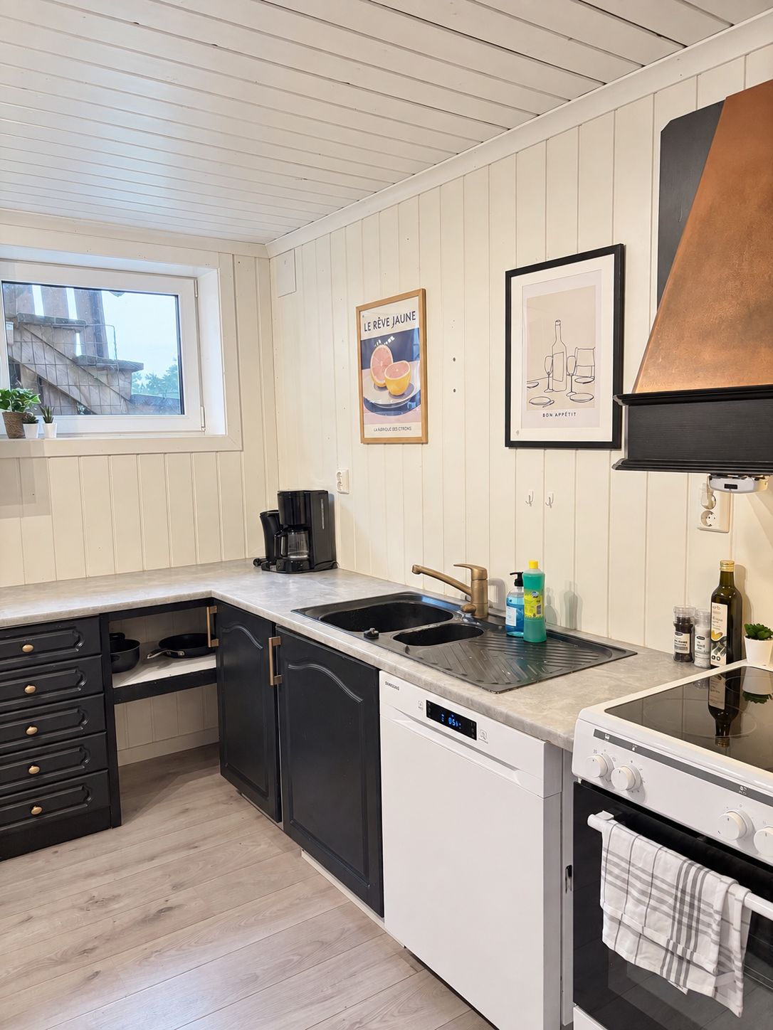 A modern kitchen with a built-in dishwasher, a stove, and a sink. There is a window providing natural light and a view of the outside.