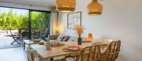 A dining area with a table set for four, surrounded by wicker chairs, under two hanging lamps.