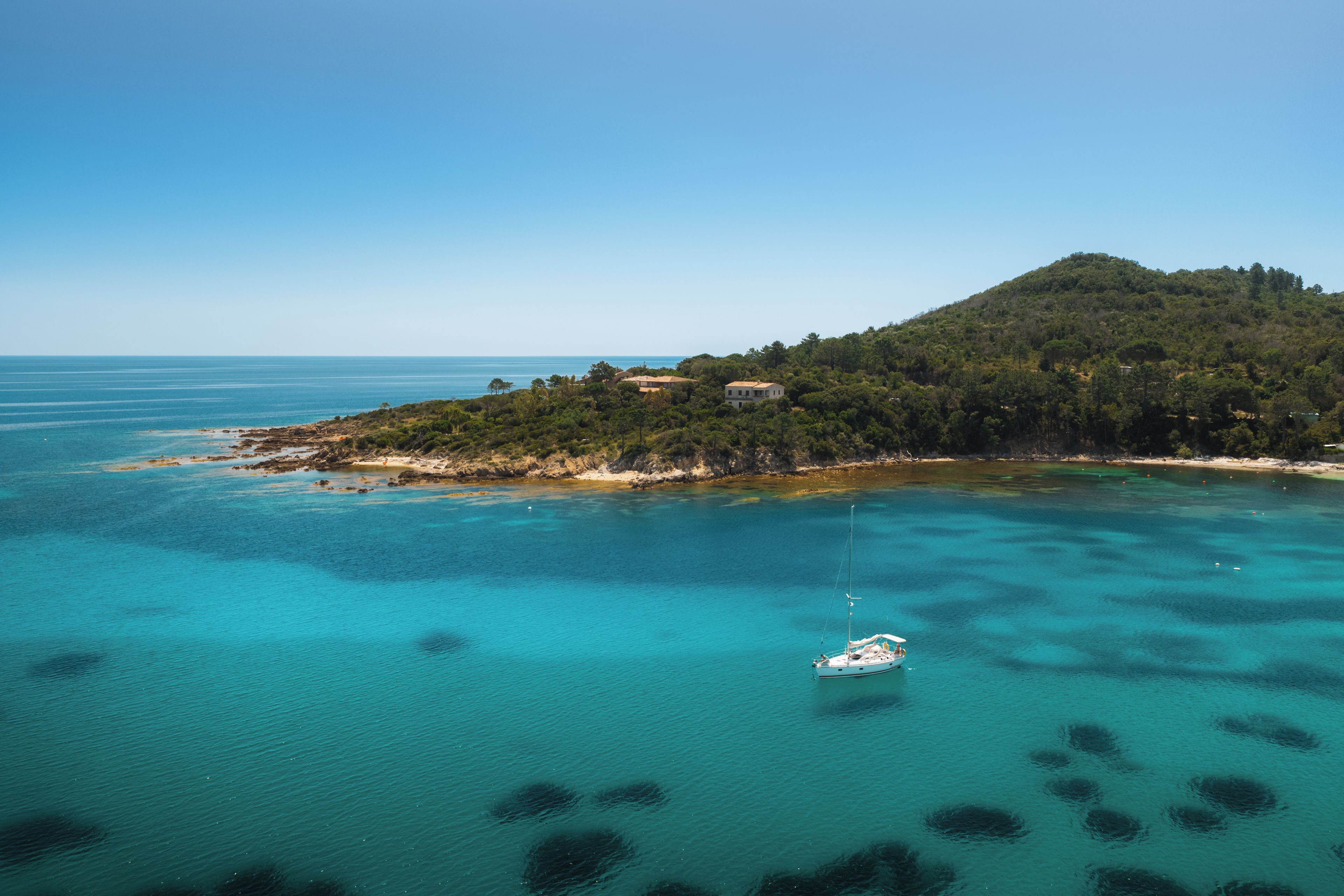 Un paisaje costero con una pequeña isla, aguas turquesas cristalinas y un barco.