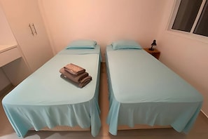 Huoneessa on kaksi sänkyä, joissa on vaaleansiniset peitteet ja tyynyt, sekä pieni yöpöytä, jossa on lamppu.