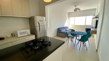 Una cocina moderna con encimera negra, armarios blancos, un refrigerador blanco y una estufa a gas. Hay una zona de comedor con una mesa azul y sillas color turquesa.