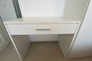 A white desk with a drawer, positioned in a corner of a room with light-colored walls and floor. - SHB - Vivendo o Sonho à Beira da Praia (Santos)