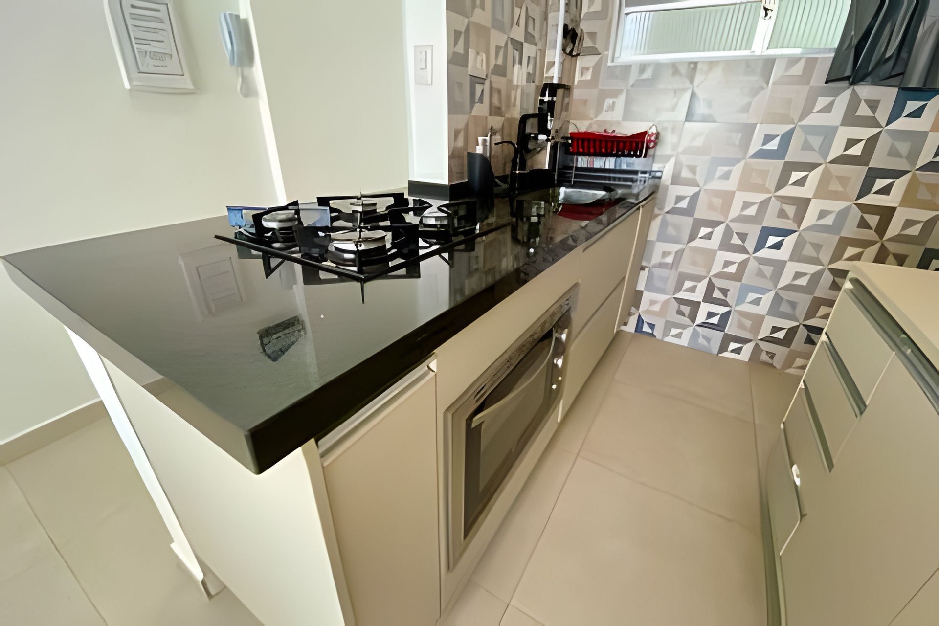 Una cocina compacta con encimera negra, electrodomésticos de acero inoxidable y un salpicadero con diseño.