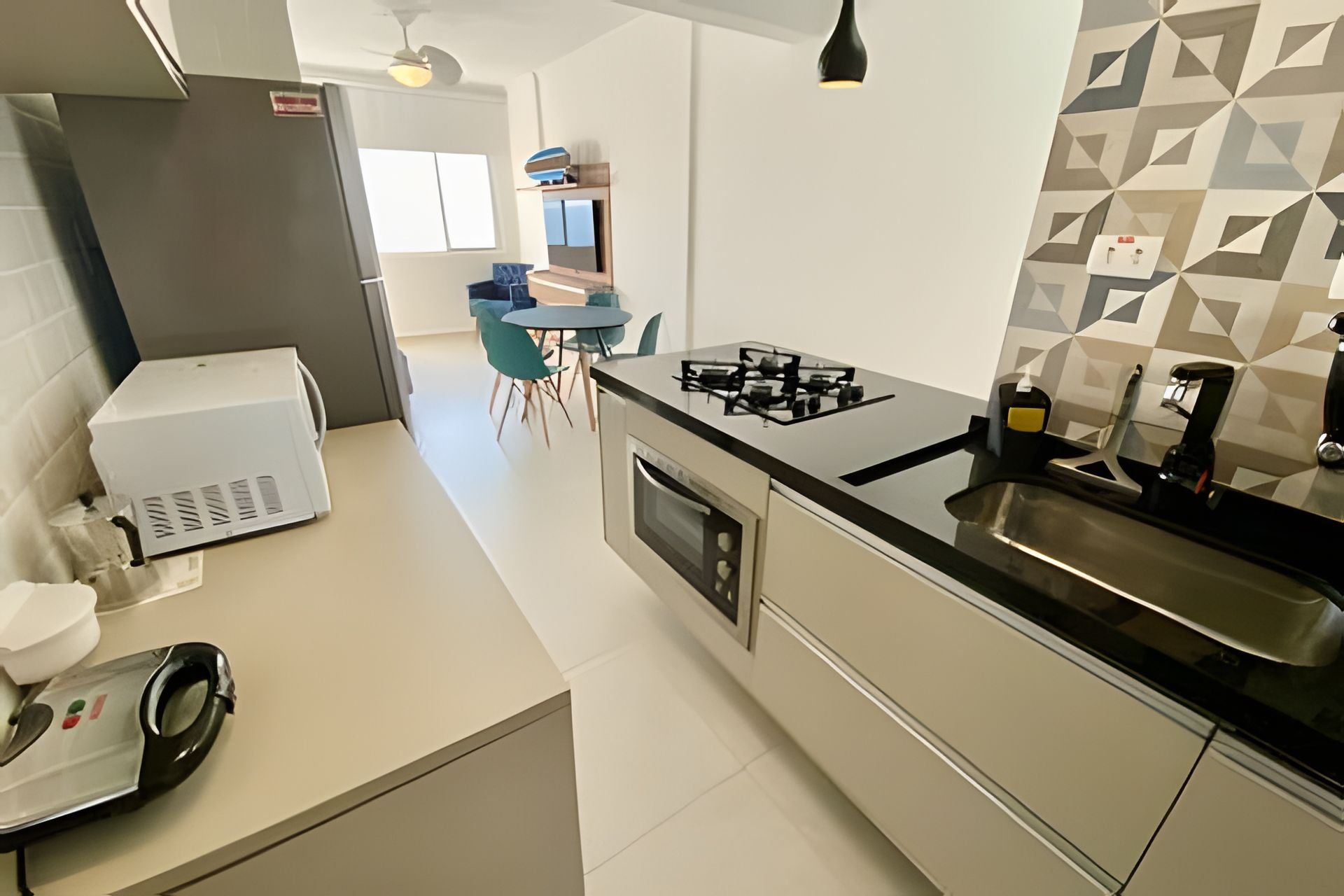 Una cocina moderna con horno empotrado, estufa a gas y un lavamanos. Se ve un comedor con una mesa y sillas al fondo.