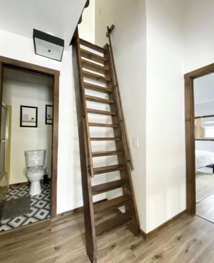 A wooden ladder in a room with a tiled floor, a white door, and a white wall.