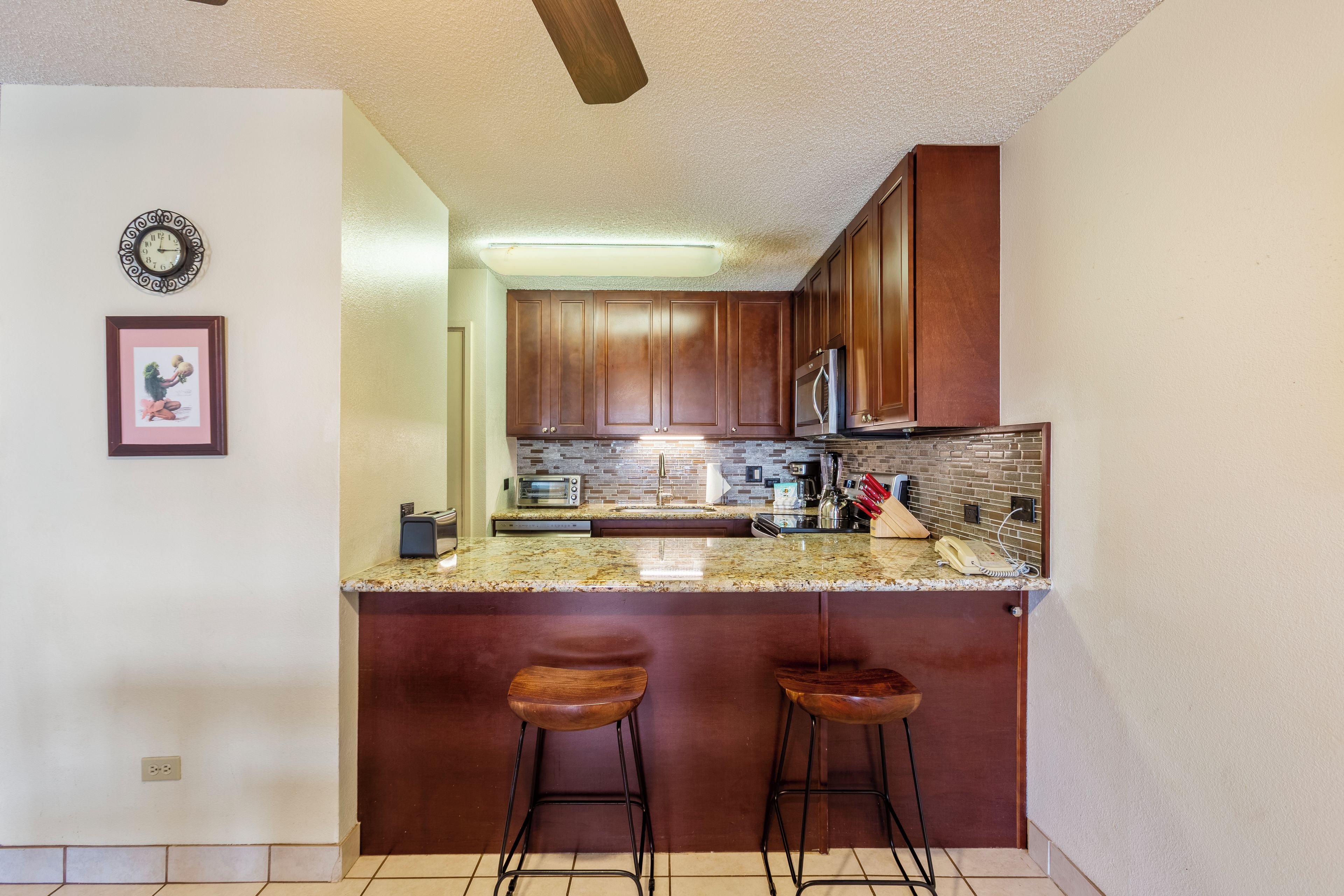 A kitchen with a granite countertop, wooden cabinets, a built-in oven, and a stainless steel refrigerator.