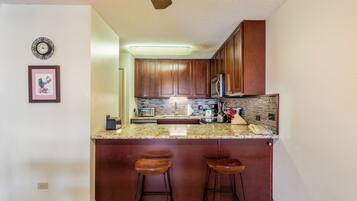 A kitchen with a granite countertop, wooden cabinets, a built-in oven, and a stainless steel refrigerator.