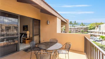 A balcony with a table and chairs, a sliding glass door, and a view of a residential area with palm trees and buildings.
