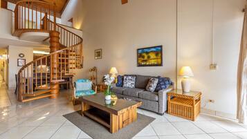 A spacious living area with a wooden staircase, a sofa set, a coffee table, and a painting on the wall.