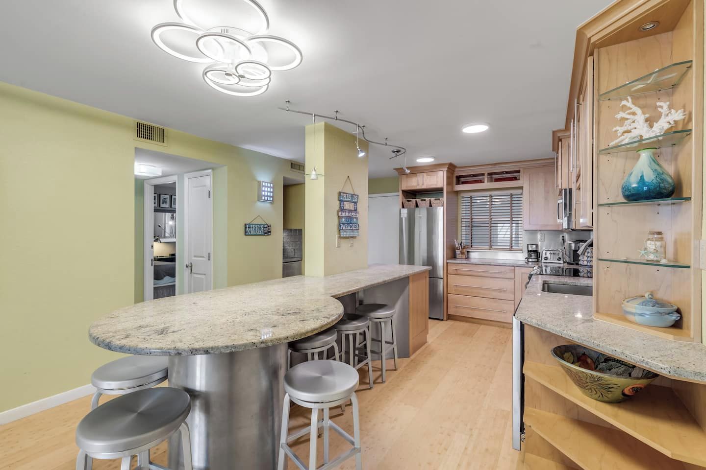 Una cocina con una isla central, taburetes de bar, electrodomésticos de acero inoxidable y un mueble de madera decorado con objetos.