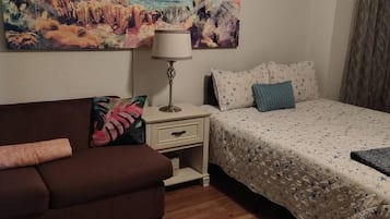 Ein Schlafzimmer mit einem Bett, einem Nachttisch, einer Lampe, einem Sofa und einem Wandbild.